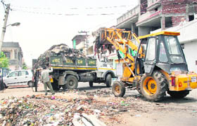 A bulldozer of the Jammu Municipal Corporation removes garbage from a busy locality in Shastri Nagar on Friday. 