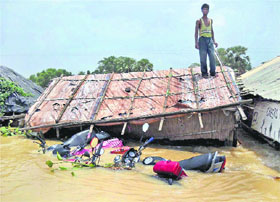 A man stands atop his thatched house in his flooded village at Ghatal in West Midnapore district of West Bengal on Tuesday