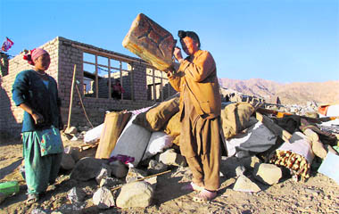 Women with their belongings outside an under-construction house being built for them in a new area after they were displaced by last year's flash floods in Choglamsar on the outskirts of Leh 