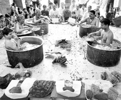 Priests perform prayers while sitting in big cooking utensils filled with water during Parjanya Varun Yagna to invoke the rain god in Ahmedabad on Sunday.