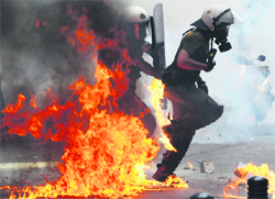 Riot police personnel advance through the flames from a molotov cocktail during protests against austerity measures in Athens on Tuesday