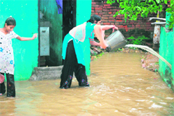 A resident of Preet Nagar area clears water from her house after heavy rain in Jammu on Thursday.