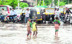 Children wade through a water-logged road as motorists wait for the rainwater to recede at Dogra Chowk in Jammu on Friday