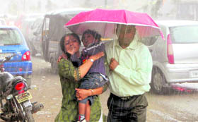 A couple and their child take cover under an umbrella during rain in Dehradun on Sunday. 
