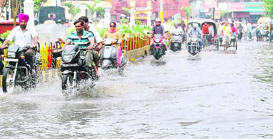 Motorcyclists navigate through the rainwater that accumulated on the road outside the Municipal Corporation office in Jalandhar 