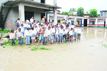 Children stand on the waterlogged primary school campus at Bhangrotu in Mandi on Thursday.