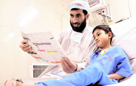 Ahabdus Samad, father of Ahamd, entertain his son by reading an Urdu newspaper at DMC Hospital in Ludhiana on Friday.