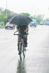 A man carrying an umbrella cycles his way to home in Jammu on Monday. 
