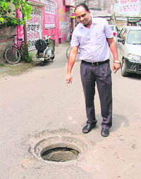 The victim, Viji Raj, shows the open manhole in Madhuban Enclave area where the front wheel of his motorcycle got stuck on Tuesday evening. 