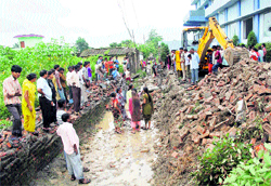 An earth-moving machine clears the debris of a wall that collapsed in the Mohhebewala area of Dehradun on Thursday