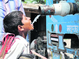 A boy quenches his thirst from a water tanker parked along a road in Nuh.