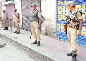 Security personnel stand guard in front of closed shops in Srinagar on Wednesday