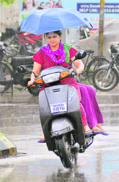 Girls on a scooter use an umbrella to protect themselves from rain in Jalandhar on Thursday.