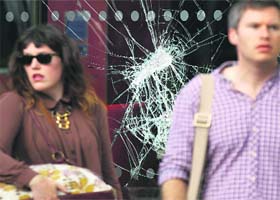 Pedestrians stand near a broken window outside a McDonalds restaurant after overnight looting in Brixton, south London, on Monday