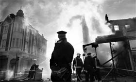 A police officer patrols as firemen continue to douse down buildings set alight during riots in Tottenham, north London, on August 7, 2011.