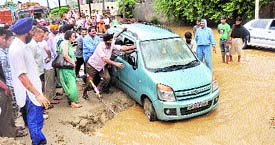 Passersby push a car out of a puddle near Tiger Safari in Ludhiana.