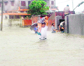 A man wades through waist-deep water carrying a child in the Clementown area of Dehradun on Tuesday. 