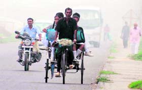 A rickshaw-puller ferries schoolchildren during the seasons first fog on the national highway in Karnal on Thursday morning.