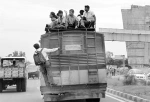 Commuters sit on the roof of a mini bus, with a man hanging on its rear side, at Zirakpur on the Chandigarh-Ambala highway.