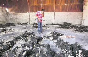 A rebel fighter looks at burnt bodies at the Khamis 32 military encampment in southern Tripoli on Sunday