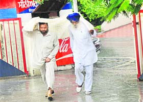 Two men use a piece of cloth to protect themselves from rain in Jalandhar on Monday