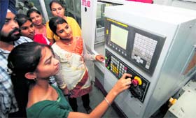 Girls learn functions of a computer numerically control vertically milling machine. 
