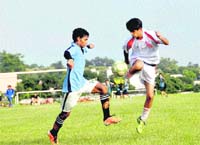 Players of Doon International School (in white) and Col Brown School (in blue) vie for the ball in a match in the RIMC Soccer Cup in Dehradun on Monday. 