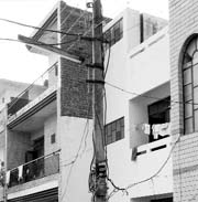 An electricity pole within the boundary wall of a house, with wires dangling dangerously