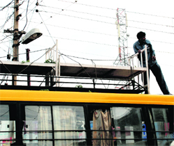 With a mesh of wires dangling overhead, a man standing on the roof a bus carries stretchers atop a bus at Sector 11, Panchkula