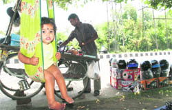 A child rests on a swing while his father busy arranging his roadside shop near Panama Chowk in Jammu. 