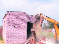 A JCB machine brings down an illegal structure in an unauthorised colony near Makrauli village in the district on Tuesday.