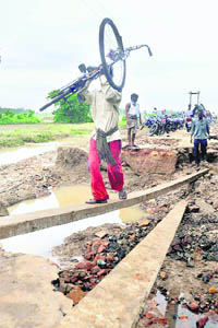 People cross a washed off road with help of concrete slabs in flood-hit Gop village of Puri district on Friday