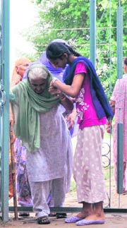A girl helps a woman cross the entry gate of Government School in Gill village