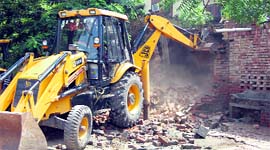 A JCB machine pulls down an illegal structure in the Samalakha grain market on Monday.