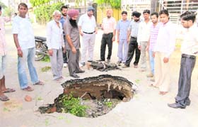 Residents look at the portion of the Pakhowal road, which caved in near Vikas Nagar in Ludhiana on Monday