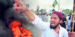 A supporter of Mumtaz Qadri (inset), the confessed killer Punjab Governor Salmaan Taseer, chants slogans next to burning tyres during a rally to condemn the court decision against Qadri in Rawalpindi on Saturday.