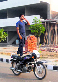 Deepak rides his motorcycle in a standing posture at Fatehabad