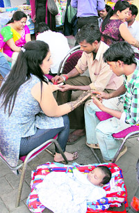 A woman gets mehndi applied on her hands as her child sleeps peacefully at a roadside stall on the eve of Karva Chauth in Jalandhar on Friday