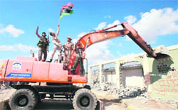 An anti-Gaddafi fighter waves a Kingdom of Libya flag as a bulldozer destroys the residence of Muammar Gaddafi at the Bab al-Aziziya complex in Tripoli.