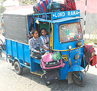 An auto-rickshaw carrying schoolchildren with their bags hung on a special perch.