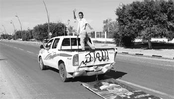 Anti-Gaddafi fighters gesture as they ride in a vehicle, trailed by an image of Muammar Gaddafi, after the fall of Sirte in the town October 20, 2011.