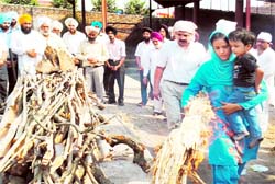 Neelu Maan lights the funeral pyre of her father, while holding her son in her arm, at the cremation ground of Gurdwara Shaheeda Sahib in Amritsar on Saturday