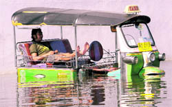 A Thai tuk tuk driver sits in his submerged vehicle in a flooded area in Bangkok on Thursday