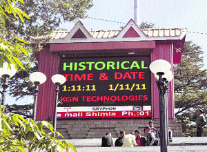 Boys sit in front of a digital screen which shows and interesting combination of date and time at the historic Ridge in Shimla on Tuesday. 