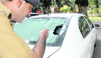 A cop points towards the smashed windowpane of the car belonging to Darshan Singh