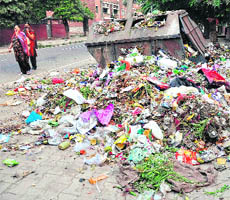 Women cover their face as they pass by a heap of garbage, which remains uncollected for days, in Sector 20, Chandigarh