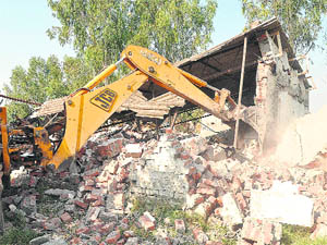 A JCB machine razes an illegal structure during a demolition drive carried out by the estate office at Maloya village, Chandigarh, on Friday.