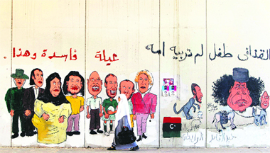 A woman walks past caricatures of former Libyan leader Muammar Gaddafi and his family on a wall in Tripoli on Sunday.