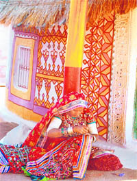 A village woman creating a bright appliqu in front of her decorated hut