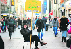 A man holds a sales board in the O'Connell Street shopping district as pedestrians walk past retail stores in Dublin. Ireland's Prime Minister Enda Kenny was set to announce a 3.8 billion euro austerity budget on Monday, a day after warning citizens to brace for years of economic hardship during a historic TV address.